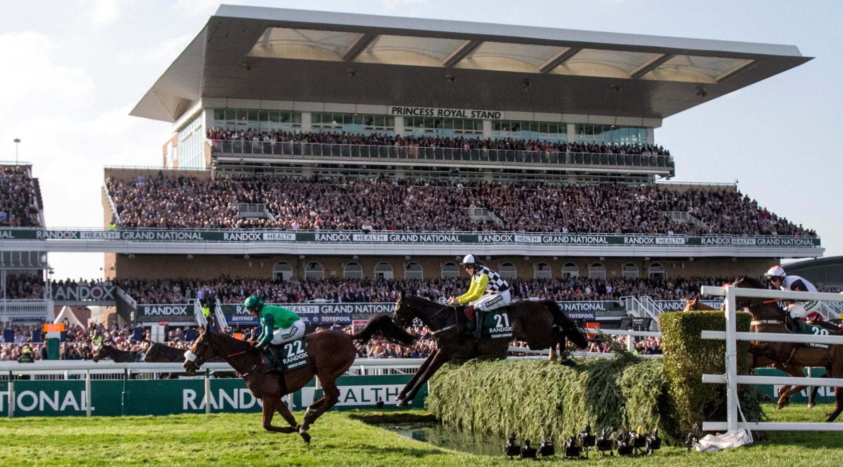 Grand National horses and riders race over the grandstand water jump fence at Aintree.